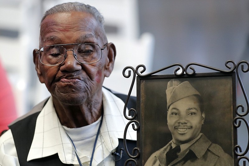 FILE - In this Sept. 12, 2019 file photo, World War II veteran Lawrence Brooks holds a photo of him taken in 1943, as he celebrates his 110th birthday at the National World War II Museum in New Orleans. Brooks celebrated his 112th birthday, Sunday, Sept. 12, 2021 with a drive-by party at his New Orleans home hosted by the National War War II Museum. Drafted in 1940, Brooks was a private in the Army's mostly Black 91st Engineer Battalion. (AP Photo/Gerald Herbert, File)