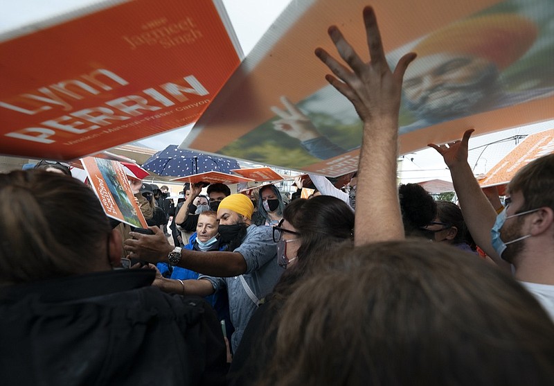 New Democratic Party supporters use signs as rain shields as NDP Leader Jagmeet Singh greets people during a campaign stop in Pitt Meadows, British Columbia, Sunday, Sept. 19, 2021. (Jonathan Hayward/The Canadian Press via AP)