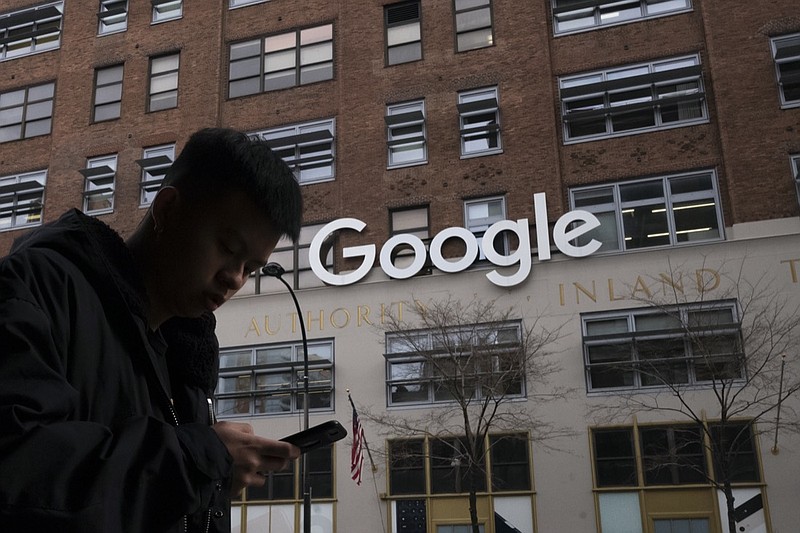 FILE - In this file photo dated Monday, Dec. 17, 2018, a man using a mobile phone walks past Google offices in New York. Google is planning to buy New York's St. John's Terminal for $2.1 billion, making it the anchor of its Hudson Square campus.Alphabet and Google Chief Financial Officer Ruth Porat said Tuesday, Sept. 21, 2021, that the company is looking to invest more than $250 million in its New York campus this year. (AP Photo/Mark Lennihan, FILE)