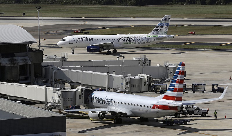 A JetBlue Airbus A320 taxis to a gate Wednesday, Oct. 26, 2016, after landing as an American Airlines jet is seen parked at its gate at Tampa International Airport in Tampa, Fla. The Justice Department is suing to stop American Airlines and JetBlue from coordinating their flights in the Northeast. Government antitrust lawyers said Tuesday, Sept. 21, 2021, that the deal between the two airlines will reduce competition and lead to higher fares. (AP Photo/Chris O'Meara, File)