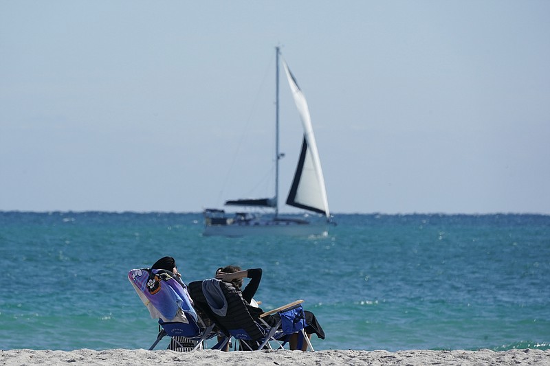 FILE - In this Dec. 1, 2020 file photo, beachgoers enjoy a chilly day at the beach as a sailboat passes by in Miami Beach, Fla. Vacation home rentals are increasingly popular among travelers, especially during the pandemic. The problem for many savvy travelers is that it's hard to use rewards points to cover the rental cost. (AP Photo/Wilfredo Lee, File)