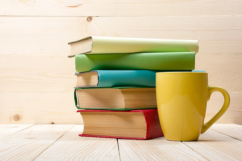Stack of colorful books and cup on wooden table.
