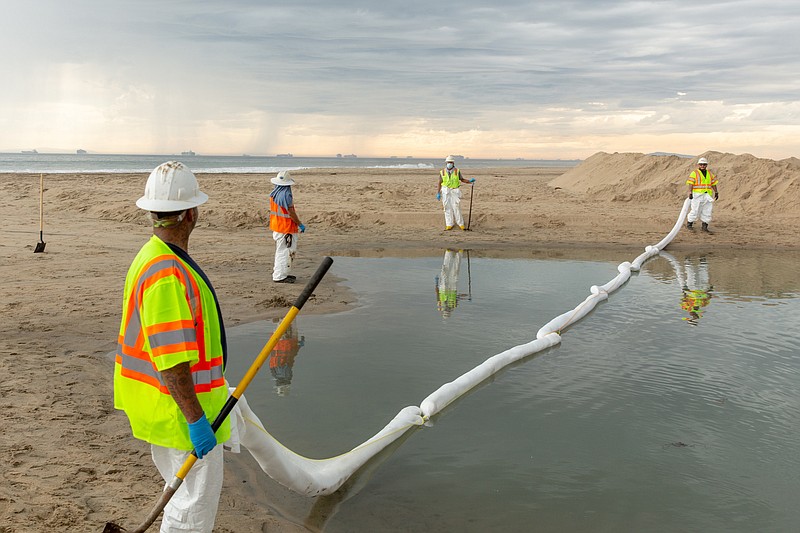 Photo by Allison Zaucha of The New York Times / Workers use an absorbent boom to clean oil out of the water in Newport Beach, Calif., on Monday, Oct. 4, 2021, following a pipeline failure off the coast that caused tens of thousands of gallsons of oil to spill into the Pacific Ocean.