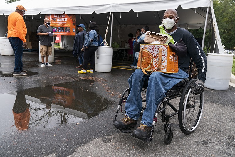 Randy Horton, of Washington, holds bags of food in his lap as he leaves in his wheelchair after receiving a bag of produce and a lunch meal at the Town Hall Education Arts & Recreation Campus (THEARC), Wednesday, Oct. 6, 2021, in Washington. (AP Photo/Jacquelyn Martin)