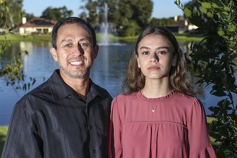 Portrait of Mitch Arbelaez and his daughter Jayden in Jacksonville, Fla., Wednesday, Oct. 13, 2021.  Banned from the Florida hospital room where her mother lay dying of COVID-19, Jayden Arbelaez pitched an idea to construction employees working nearby.  The workers gave the 17-year-old a yellow vest, boots, a helmet and a ladder to climb onto a section of roof so she could look through the window and see her mother, Michelle Arbelaez, alive one last time. (AP Photo/Gary McCullough)