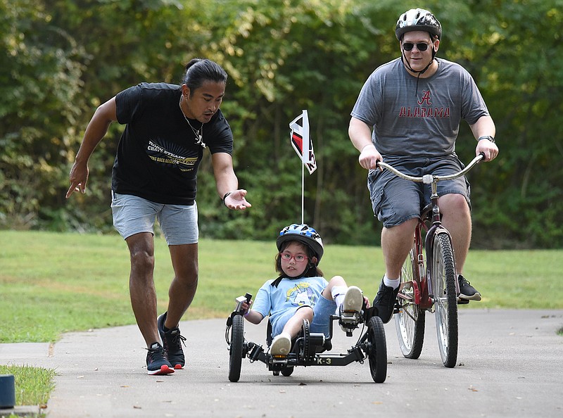 Staff Photo by Matt Hamilton / Volunteer Jake Aragon, left, helps Rossville resident Libby Leonard, 11, as she bikes with her dad Charlie at the Tennessee Riverpark Northern Amnicola Marsh Site.