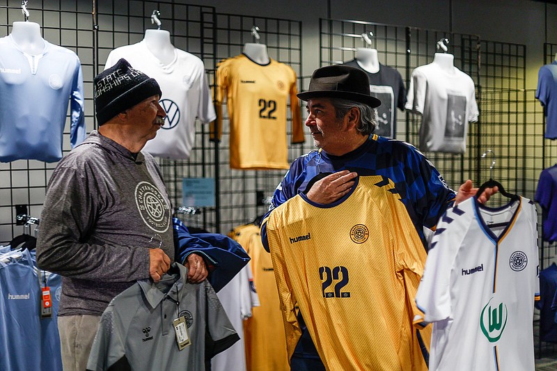 Staff photo by Troy Stolt / William Disk, left, speaks with Chattanooga FC part owner Ron Burkett as he holds a special edition gold CFC jersey's at the team's merchandise shop in Finley Stadium on Wednesday night.