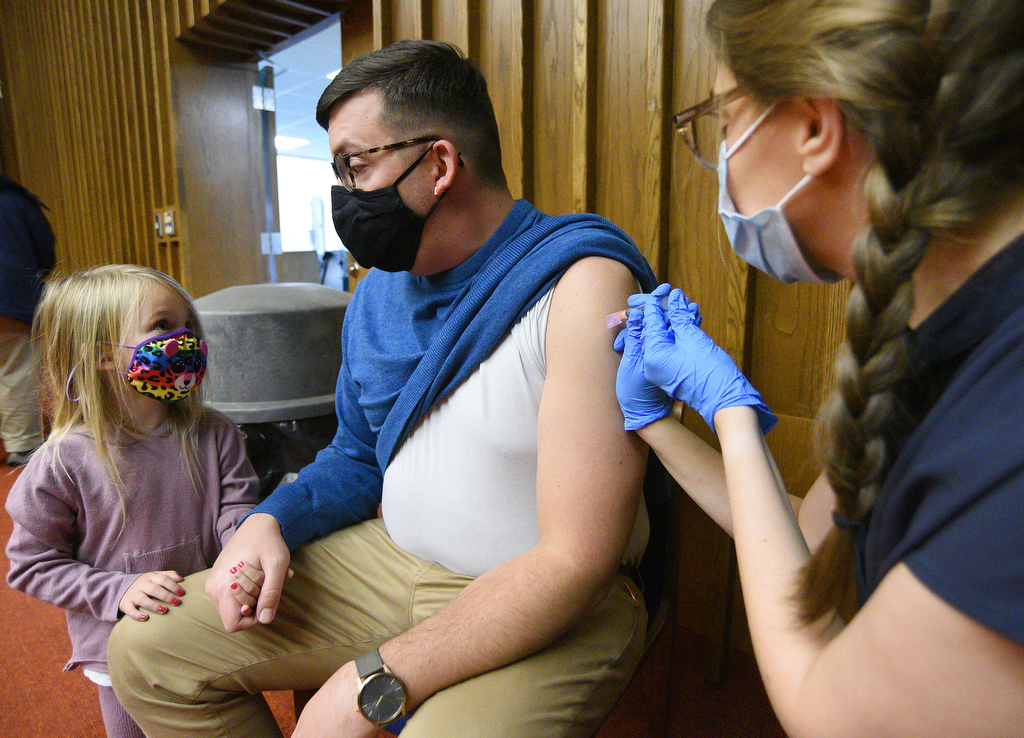 Staff Photo by Matt Hamilton / Chattanooga resident Isla Holland, 4, holds the hand of her dad, Matt, as he gets his COVID booster shot from nurse practitioner Meghan Whitehead on Friday, November 13, 2021 at the downtown branch of the Chattanooga Public Library. Lifespring Community Health was providing vaccination shots to children as young as five years old on Friday.