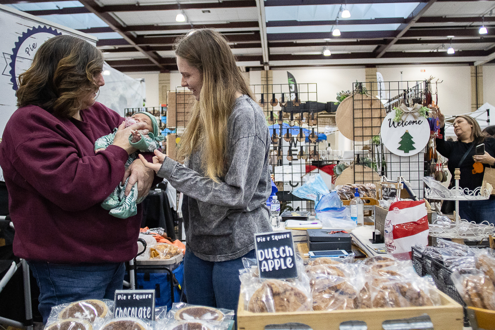 Staff photo by Troy Stolt / Patricia Travis and Julia Valentine hold 8-month-old Olive Dickerson at their booth during the Holiday Market at the Chattanooga Convention Center on Saturday, Dec. 11, 2021.