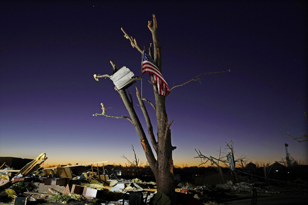 An American flag hangs from a damaged tree Sunday, Dec. 12, 2021, in Mayfield, Ky. Tornadoes and severe weather caused catastrophic damage across several states Friday, killing multiple people. (AP Photo/Mark Humphrey)