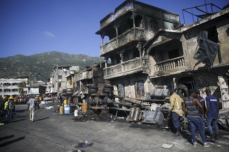 Firefighters stand next to what remains of a truck that was carrying gasoline after it overturned and exploded in Cap-Hatien, Haiti, Tuesday, Dec. 14, 2021. The explosion engulfed cars and homes in flames, killing more than 50 people and injured dozens of others. (AP Photo/Joseph Odelyn)


