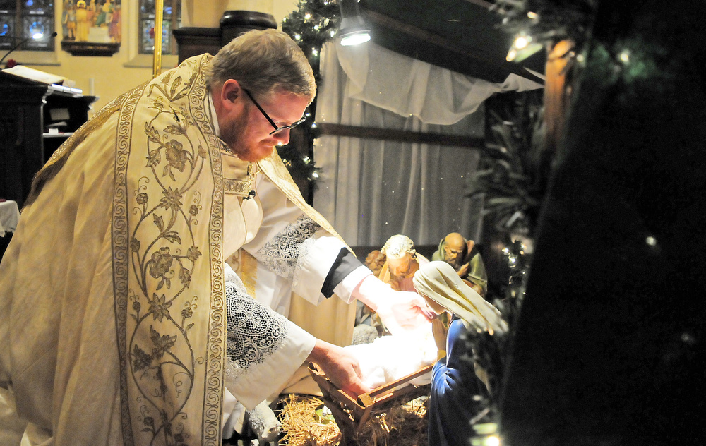 Staff Photo by Robin Rudd / The Reverend David Carter places the figure of the Christ Child in the Nativity scene. The Vigil Mass of Christmas was celebrated at the Basilica of Saints Peter and Paul on December 24, 2021.