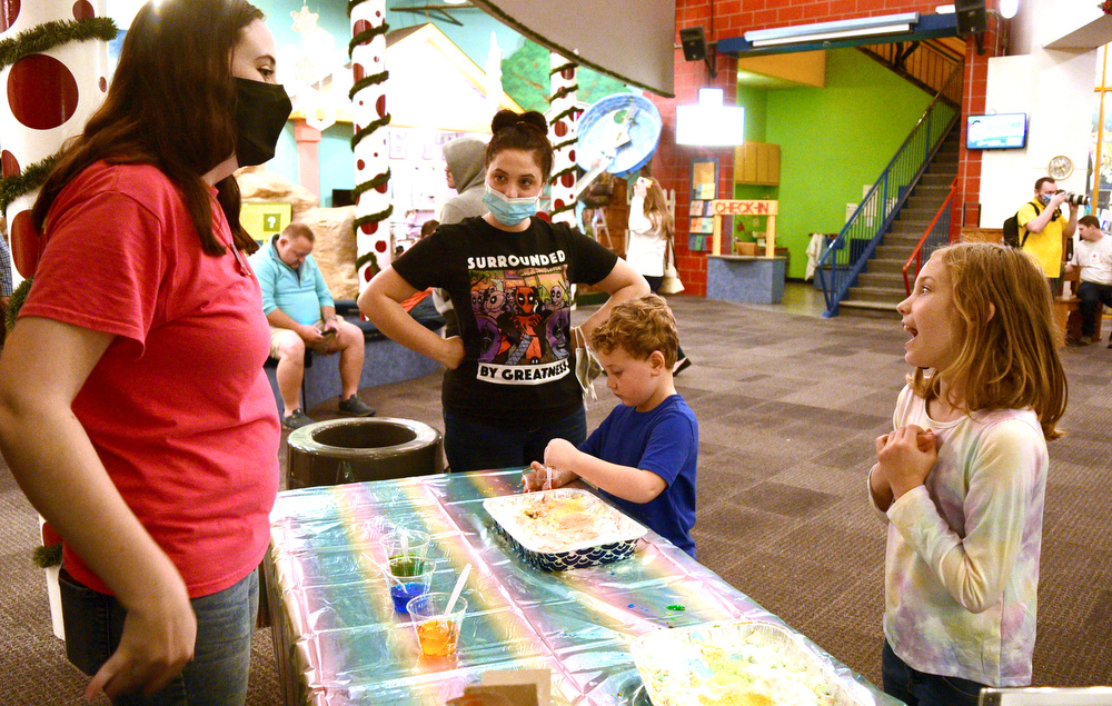 Staff Photo by Robin Rudd / At the Flizzing Colors Work Station, museum staffer Fiona Coleman, left, talks with Ava Harper about their favorite dinosaurs, while brother August works on his cake, and mom, Kimberly watches. The New Year was celebrated during the "Cheers for the New Year" event at the Creative Discovery Museum on December 30, 2021.