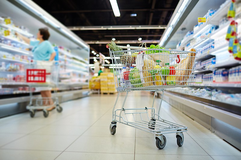 Shopping cart full of grocery standing next to shelves. / Getty Images/iStock/shironosov