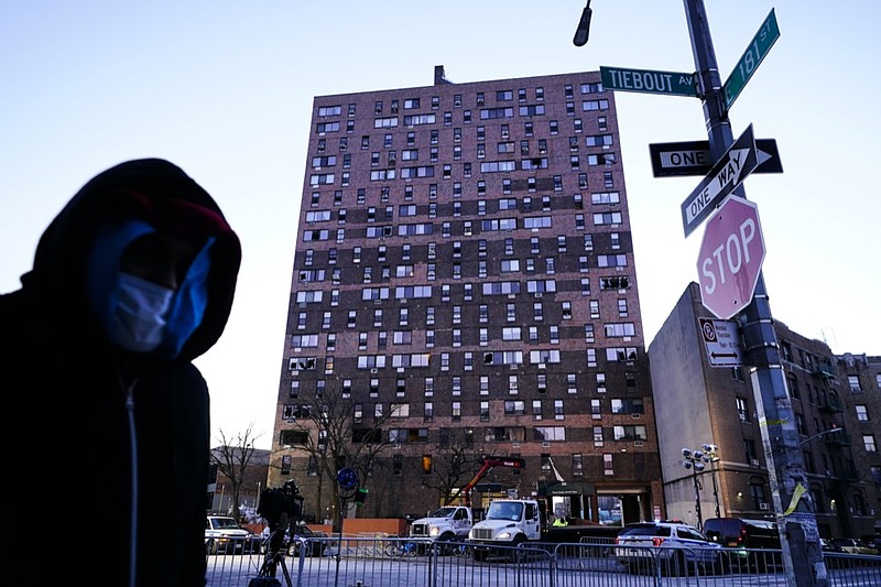 A person walks past an apartment building which suffered the city's deadliest fire in three decades, in the Bronx borough of New York, Tuesday, Jan. 11, 2022. A malfunctioning electric space heater apparently started the fire Sunday in the 19-story building in the Bronx, fire officials said. (AP Photo/Matt Rourke)
