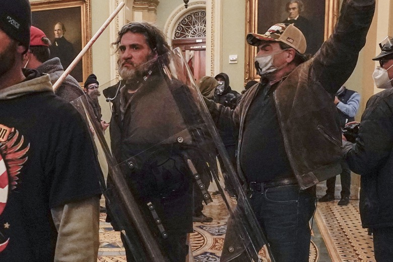 In this Jan. 6, 2021, photo, rioters, including Dominic Pezzola, center with police shield, are confronted by U.S. Capitol Police officers outside the Senate Chamber inside the Capitol, Wednesday, Jan. 6, 2021, in Washington. The Proud Boys and Oath Keepers make up a fraction of the more than 300 Trump supporters charged so far in the siege that led to Trump's second impeachment and resulted in the deaths of five people, including a police officer. But several of their leaders, members and associates have become the central targets of the Justice Department’s sprawling investigation. (AP Photo/Manuel Balce Ceneta)