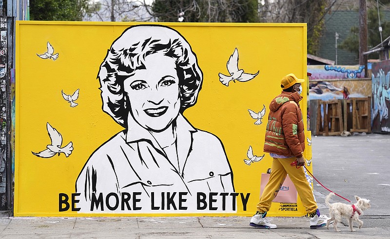 A man walks a dog past a new mural of the late actress Betty White by artist Corie Mattie, Tuesday, Jan. 13, 2022, in Los Angeles. Mattie added a QR code to the mural so people walking by can donate to the local shelter Wagmor Pets Dog Rescue in honor of White, an animal welfare advocate. White died Dec. 31 at age 99. (AP Photo/Chris Pizzello)