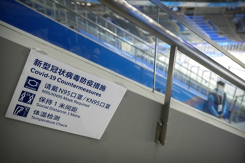 FILE - A staff member stands near a sign outlining COVID-19 protection measures during the Experience Beijing Ice Hockey Domestic Test Activity, a test event for the 2022 Beijing Winter Olympics, at the National Indoor Stadium in Beijing, on Nov. 10, 2021. (AP Photo/Mark Schiefelbein, File)


