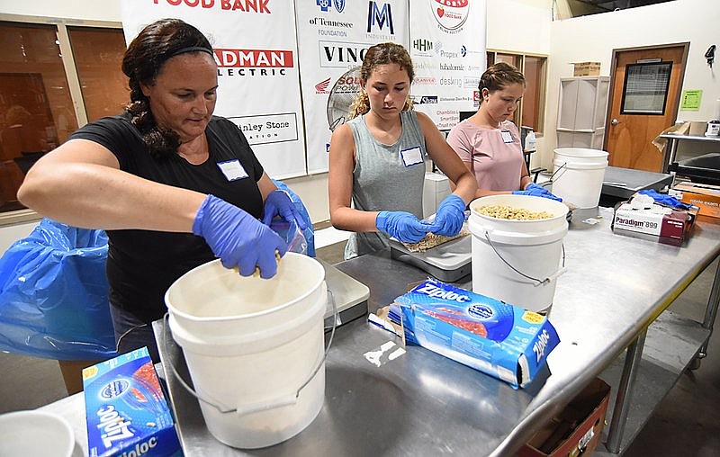 Staff Photo by Matt Hamilton / Martha Carpenter, left, works with her daughters Caroline, 13, middle, and Abigail, 14, as they bag bulk elbow pasta at the Chattanooga Area Food Bank on Tuesday, July 6, 2021. The group was working to repackage an 1,100-pound box of pasta into 16-ounce bags.