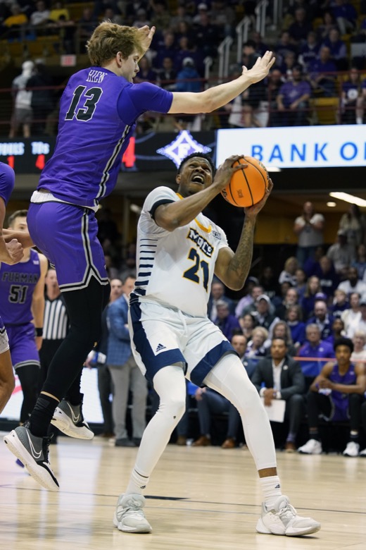 Furman forward Garrett Hien (13) leaps to block Chattanooga forward Josh Ayeni's (21) shot at the basket in the first half of an NCAA college basketball championship game for the Southern Conference tournament, Monday, March 7, 2022, in Asheville, N.C. (AP Photo/Kathy Kmonicek)