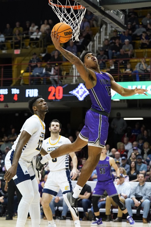 Furman forward Tyrese Hughey (15) leaps for the basket around Chattanooga forward Silvio De Sousa (22) in the first half of an NCAA college basketball championship game for the Southern Conference tournament, Monday, March 7, 2022, in Asheville, N.C. (AP Photo/Kathy Kmonicek)