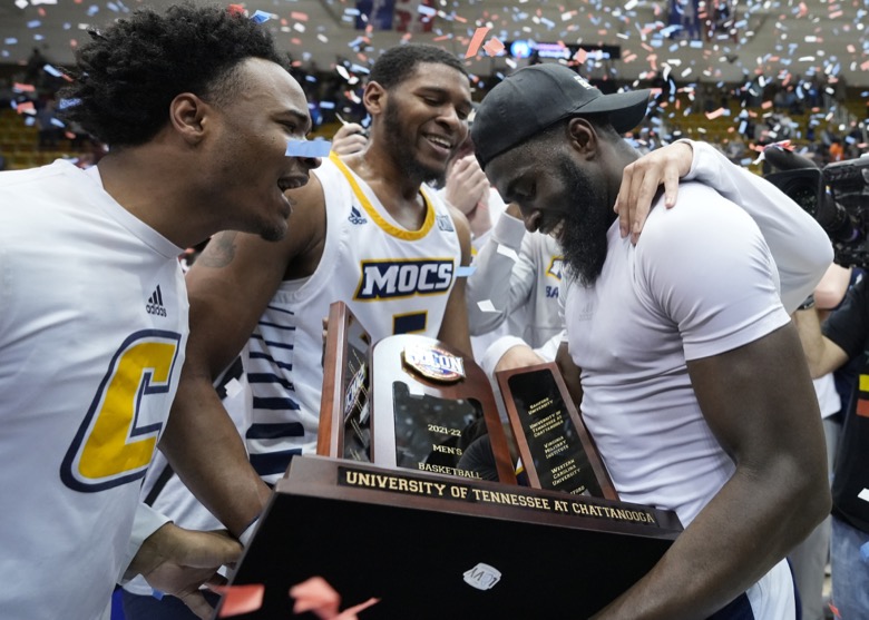 Chattanooga guard David Jean-Baptiste, right, is congratulated by teammates as he holds the championship trophy after his team defeated Furman in an NCAA college basketball championship game for the Southern Conference tournament, Monday, March 7, 2022, in Asheville, N.C. (AP Photo/Kathy Kmonicek)