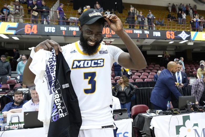 Chattanooga guard David Jean-Baptiste (3) puts on his championship cap after shooting the winning basket to defeat Furman in an NCAA college basketball championship game for the Southern Conference tournament, Monday, March 7, 2022, in Asheville, N.C. (AP Photo/Kathy Kmonicek)