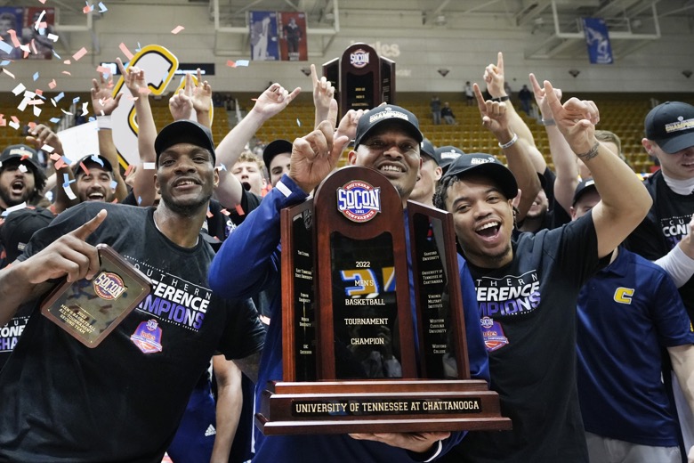 Chattanooga forward Silvio De Sousa, left, head coach Lamont Paris and guard Ashton Smith (11) hold the championship trophy to celebrate their win over Furman in an NCAA college basketball championship game for the Southern Conference tournament, Monday, March 7, 2022, in Asheville, N.C. (AP Photo/Kathy Kmonicek)