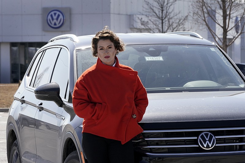 Kendall Heiman stands with the loaner car she has driven for the past two months, Wednesday, March 9, 2022, in Lawrence, Kan., while a dealership works to repair her Volkswagen 2021 Atlas Cross Sport after the car slammed on the brakes for no reason on Jan. 5. Heiman and a dozen other Cross Sport owners have filed complaints about the issues with the U.S. National Highway Traffic Safety Administration. (AP Photo/Charlie Riedel)