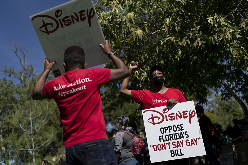 Two LGBTQ supporters hold signs to protest Disney's stance on LGBTQ issues in Glendale, Calif., Tuesday, March 22, 2022. With some workers across the U.S. threatening a walkout, The Walt Disney Co. finds itself performing a high-wire act of balancing the expectations of a diverse workforce against demands from an increasingly polarized and politicized marketplace. (AP Photo/Jae C. Hong)
