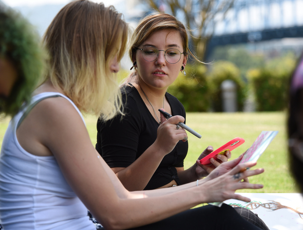 Staff Photo by Matt Hamilton / Chattanooga resident ZoԠDaniels talks with Kate Johnson, back, about their paintings as they sit in the shade in Coolidge Park on Thursday. The two met with a group of friends and decided to get together in Coolidge Park and paint together due to the weather being so mild compared to the recent hot temperatures on Thursday, August 5, 2021.