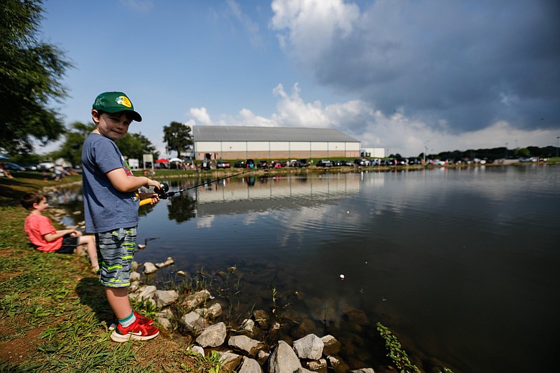 Staff photo by Troy Stolt / Avery Dixon, 8, sits as he fishes, while his brother Graham, 6, stands during The East Ridge Optimist Fishing Rodeo at Jack Dickert Fishing Pond in Camp Jordan on Saturday, June 12, 2021 in East Ridge, Tenn.