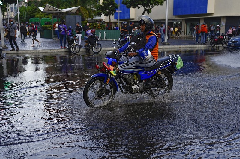 A man rides his motorcycle over a puddle in Caracas, Venezuela, Wednesday, June 29, 2022. As the latest tropical disturbance advances through the area, Venezuela shuttered schools, opened shelters and restricted air and water transportation on Wednesday as President Nicolas Maduro noted that the South American country already has been struggling with recent heavy rains. (AP Photo/Ariana Cubillos)