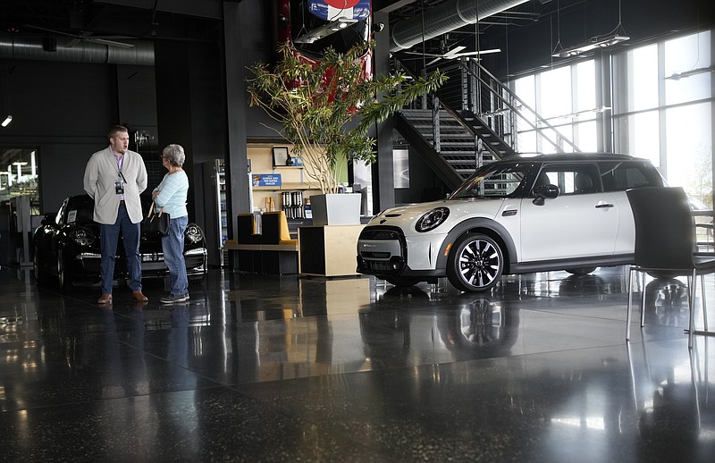 FILE - Prospective buyer chats with a sales associate as a 2022 Cooper S hardtop sits on the otherwise empty showroom floor of a Mini dealership Friday, May 6, 2022, in Highlands Ranch, Colo. As if buying a new car in today's supply-constrained market wasn't hard enough, this year, many shoppers are experiencing sticker shock when they realize that the car they wanted has a price tag well over the manufacturer's suggested retail price. (AP Photo/David Zalubowski, File)