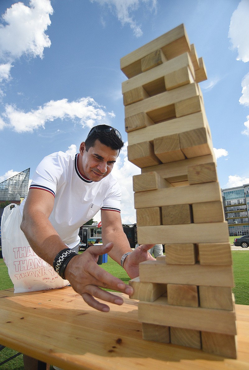 Atlanta resident Jorge Silva attempts to remove a Jenga block while playing against his daughter Isabella on Saturday, August 13, 2022 at Ross's Landing. Jenga blocks, corn hole sets and more attractions were set up along the riverfront area before the Riverfront Nights free concert Saturday. /  Staff photo by Matt Hamilton 
